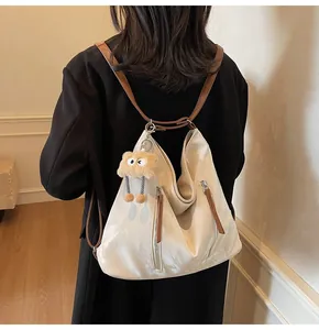 Detail of a beige tote bag with brown straps and a cute plush monster charm decoration