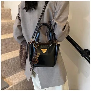 Detail of black glossy bucket bag with gold triangle logo and silk scarf pendant charm
