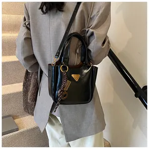 Detail of glossy black bucket bag with gold triangle logo and ornate knot charm