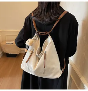 Close-up of beige nylon tote bag showing dark brown leather straps and plush bear charm