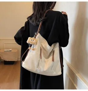 Detailed view of beige tote bag with brown straps and cute teddy bear pendant on shoulder