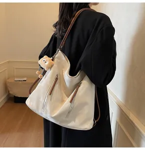 Detail of a white glossy tote bag with brown straps and a cute plush bear pendant accessory