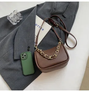 Vue à plat d'un sac à bandoulière marron texturé avec chaîne dorée et magazine