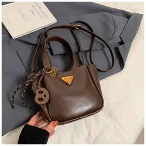 Close-up of brown oiled leather bucket bag featuring a gold triangle logo and braided charm