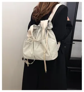 Detailed view of light grey nylon drawstring backpack worn by model in minimalist setting