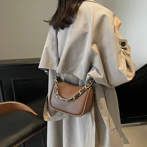 Sac à bandoulière en cuir marron avec chaîne porté avec un trench-coat beige élégant