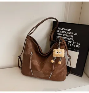 Detail of brown vintage leather tote with decorative silver zippers and plush bear charm