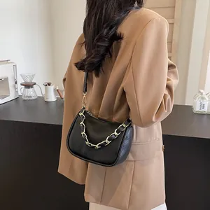 Sac demi-lune chic en cuir noir avec chaîne dorée porté par un mannequin au café