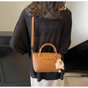 Detail of tan lychee leather handbag with plush sheep charm and crossbody strap