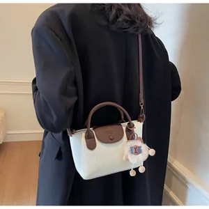 Close-up of contrast leather handle and plush sheep charm on beige crossbody dumpling bag