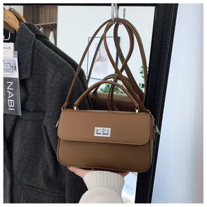 Detail of a brown leather crossbody bag featuring a silver rotary lock and handle