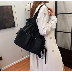 Detail view of black drawstring tote bag with front pockets and wide shoulder strap