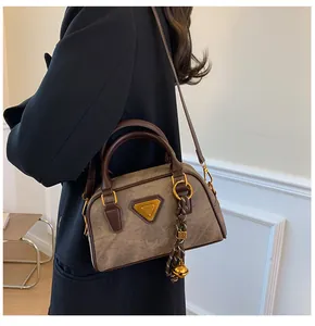 Close-up of retro Boston bag with textured leather, golden logo, and bell charm detail
