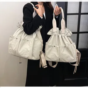 Detail of two cream nylon drawstring tote bags showing front pockets and texture