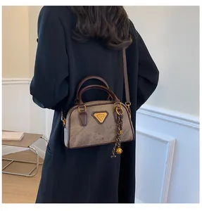 Close-up of a vintage brown Boston bag with bell charm on a model in a dark suit