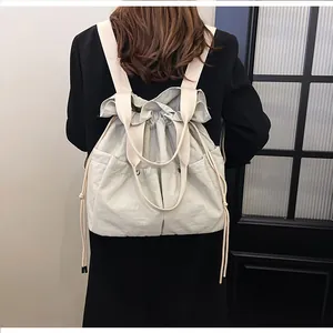 Rear view of model wearing a beige drawstring nylon backpack with large pockets