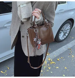 Detalle de bolso tote marrón oscuro brillante con colgante de oso y relieve