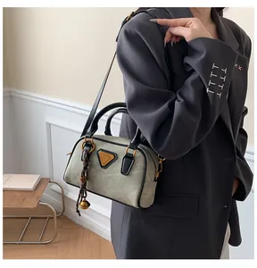 Close-up of grey suede Boston bag with gold triangle plaque and woven leather straps