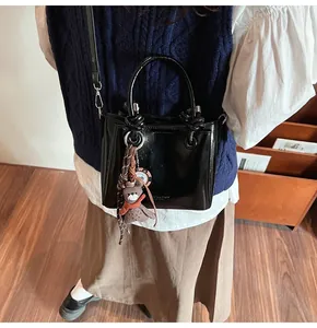 Detalle del bolso de charol negro con asa redonda y un colgante de oso adorable
