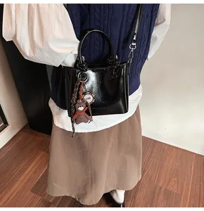 Detalle del mini bolso tote de charol negro con colgante de osito y correa metálica