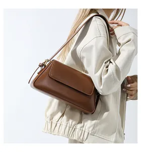 Detail view of a brown leather underarm baguette bag worn over a beige jacket