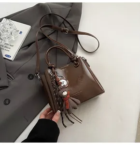 Detalle de un bolso tote marrón brillante con textura de cuero y colgante de oso