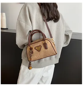 Detail of a khaki mini bowling bag with dark brown handles and golden bell charm