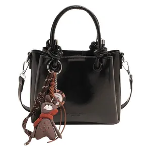 Bolso trapezoidal negro brillante con asas anudadas y colgante de conejo de peluche