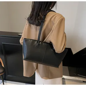Detailed side view of large black matte leather tote bag worn with khaki blazer
