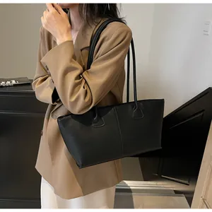 Close-up of a black textured leather tote bag worn as a shoulder bag on a model