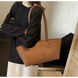 Detailed texture of a brown matte leather tote bag with vertical stitching and long strap