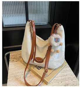 Detail of off-white tote bag featuring brown leather straps and gold chain accents