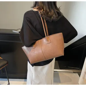 Brown leather tote bag featuring long straps for underarm carry and vertical seam detail