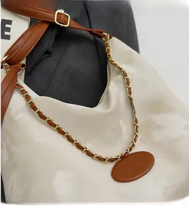 Detail of gold chain strap with brown leather tag on a cream-colored tote bag