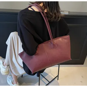 Detail of burgundy leather tote bag with long straps shown on a model for shoulder carry
