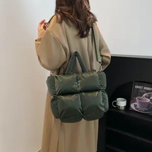 Deep green quilted puffer tote bag with wide shoulder strap on beige trench coat model