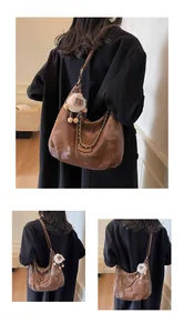 Detail of a brown glossy crescent tote bag with metal chain and white plush sheep pendant