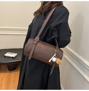 Detail einer braunen Zylindertasche mit Reliefschrift und Baseball-Anhänger
