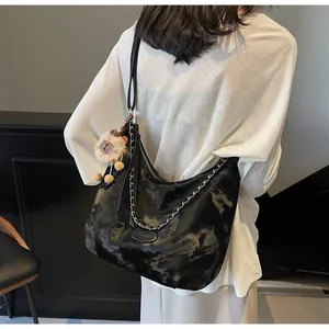 Detail of a large black glossy tote bag with silver chain and a plush lion charm