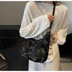 Detail of black marble textured leather tote bag with metal chain and plush charm