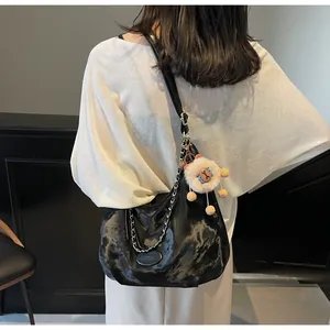 Detail of black glossy hobo bag with silver chain and cute plush sheep charm accessory