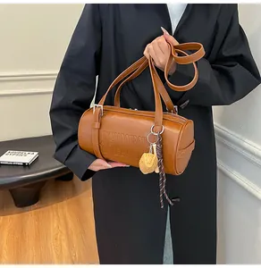 Nahaufnahme der braunen Zylindertasche mit NICHADOUDOU-Schriftzug und Baseballhandschuh-Anhänger