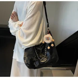 Detail of a black high-gloss tote bag with silver chain and brown plush charm accessory