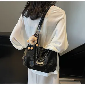 Detail of glossy black tote bag featuring silver chain and plush lion charm accessory