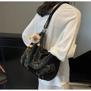Detail of black glossy leather tote with silver chain and cute brown plush charm