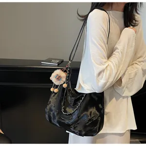 Detail view of black tote bag featuring silver chain straps and a plush lion charm