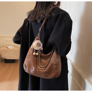 Detail of soft brown leather tote bag with metal chain and plush sheep keychain accessory