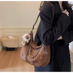 Detail of glossy brown tote bag with metallic chain strap and plush bear pendant
