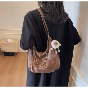 Detail of dark brown hobo bag with gold chain and plush charm on a model's shoulder
