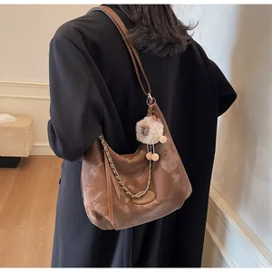 Detail of glossy brown leather tote with decorative gold chain and plush sheep pendant charm